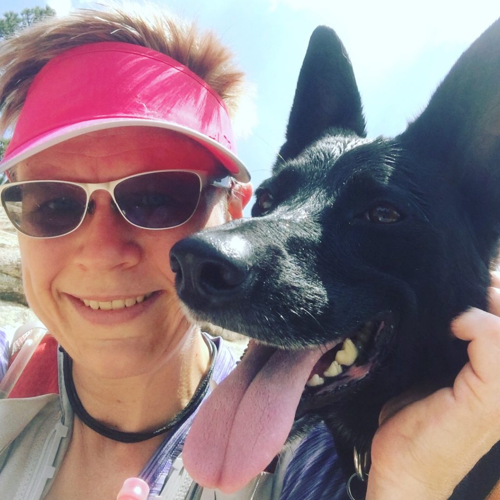 A photo of the author in running gear with her dog Nairobi, a black shepard mix with big pointy ears, shown panting.