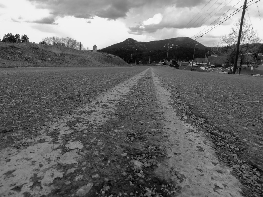 A very low angle of a road in a rural area.  The road is empty, and the camera is nearly centered on the double yellow line.  
