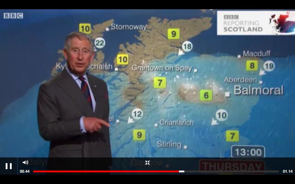 Prince Charles in front of a projected map of the UK with temperatures superimposed on it, delivering a weather forecast.  