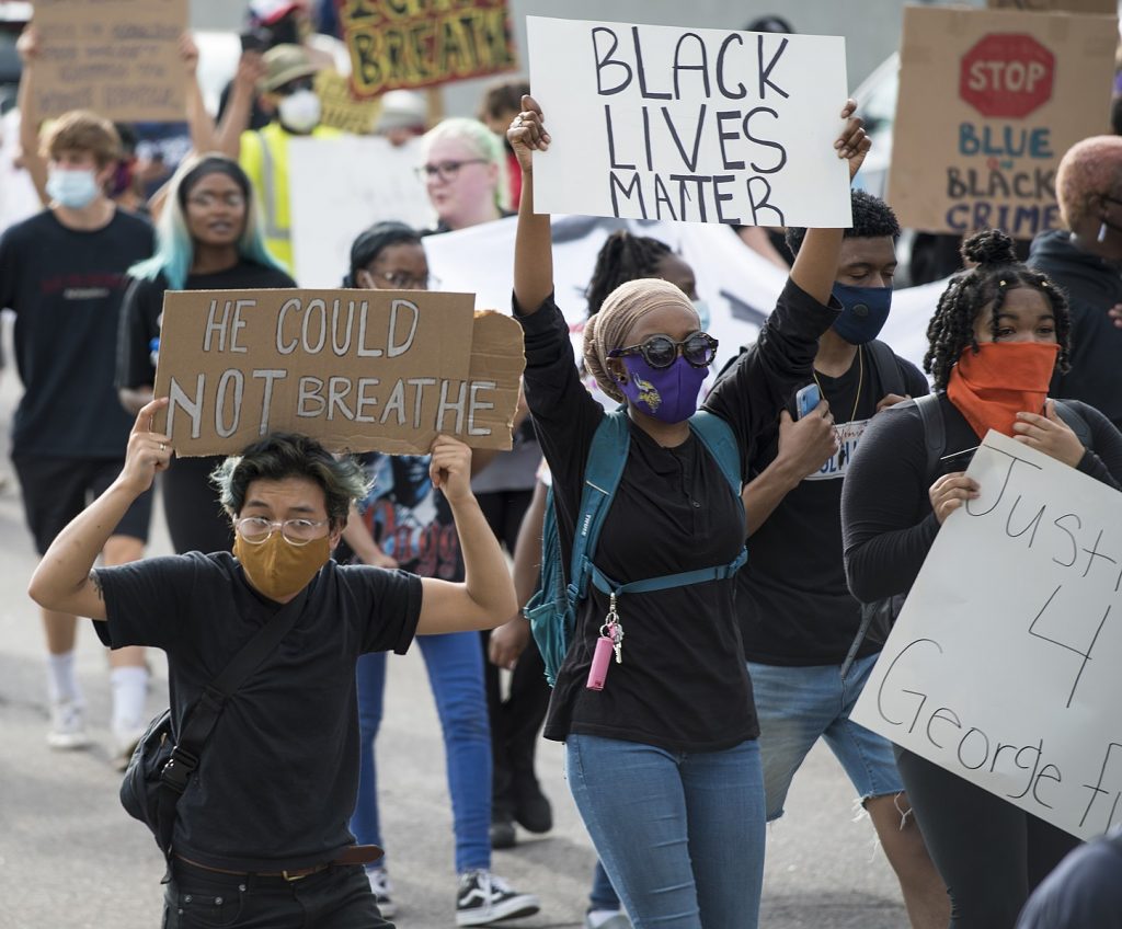 People protest with signs after the killing of George Floyd.  African-Americans feature prominently, but there is a white person and another person of color in the image as well.  Signs read "black lives matter," "he could not breathe," and "stop (sign image) blue on black crime."  