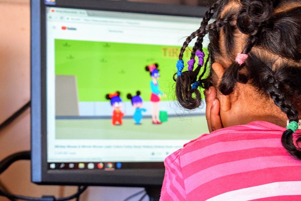 A young girl sits in front of a desktop computer screen.  She may be playing a game, or she may be in school in a distance learning sense.  