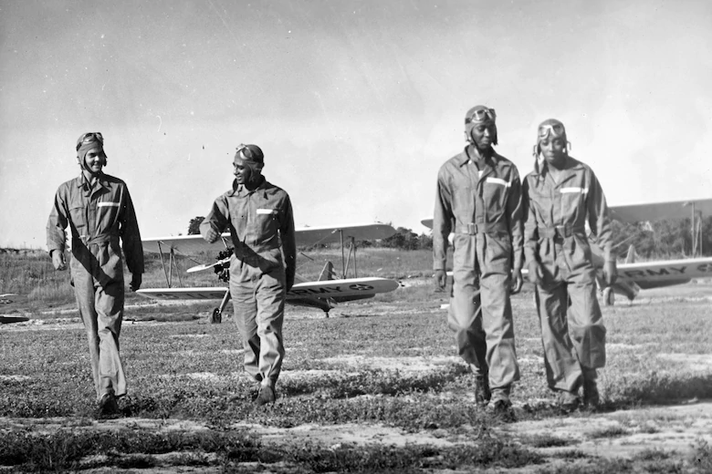 Four Tuskeegee Airmen walk across a field with two planes in the background.  We need common heroes in this country.  