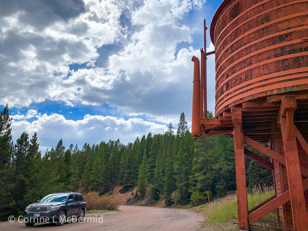 A large wooden water tank, painted orange, is on the right side of the image.  The road (Boreas Pass) comes in from the middle and goes off to the left.  You can see my car on the left, also, and lots of trees. 